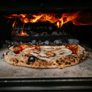 Close-up of authentic pizza cooking in a wood-fired oven with flames.