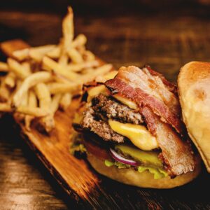 Savor a mouthwatering bacon cheeseburger with crispy fries on a rustic wooden board. Perfect fast food indulgence.