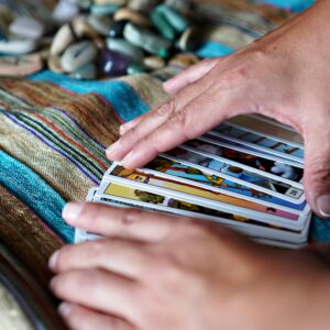 Hands arranging tarot cards on a vibrant cloth with gemstones, creating a mystical atmosphere.