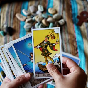 Hands holding tarot cards over a vibrant striped cloth with stones and charms, creating a spiritual atmosphere.