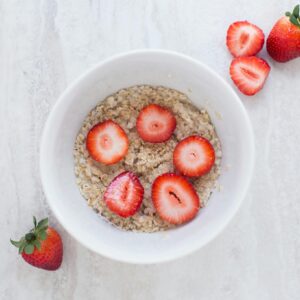 A fresh and nutritious breakfast bowl featuring oats topped with sliced strawberries.