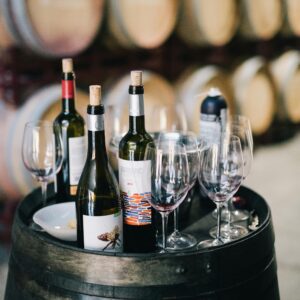 Assorted wine bottles and glasses on a barrel in a traditional winery setting.
